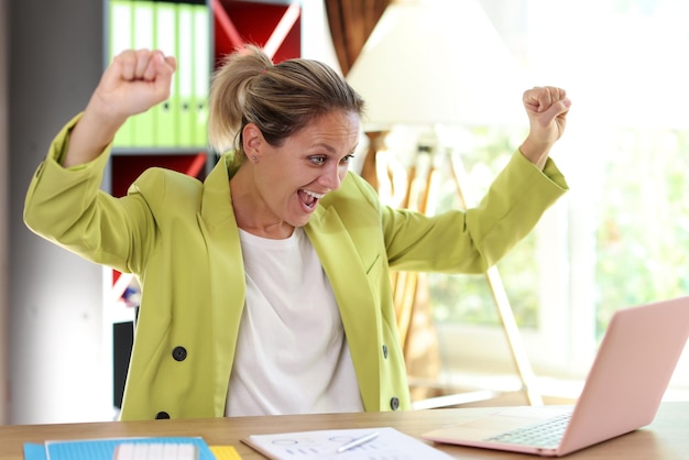 Heureuse femme d'affaires excitée avec les mains levées et une femme caucasienne pour ordinateur portable la célèbre