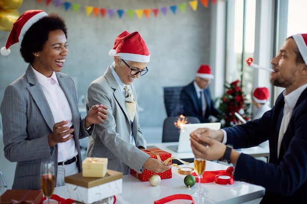 Heureuse femme d'affaires mature et ses collègues s'amusant tout en emballant des coffrets cadeaux pour la fête de Noël