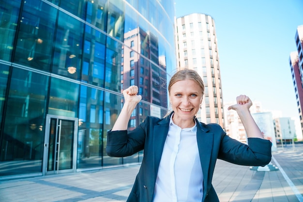 Heureuse femme d'affaires montrant les pouces vers le haut tout en se tenant à l'extérieur contre le bureau