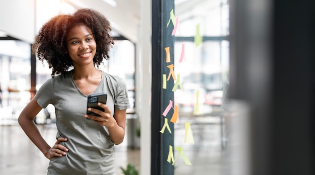 Heureuse femme d'affaires noire à l'aide d'un smartphone dans un bureau créatif