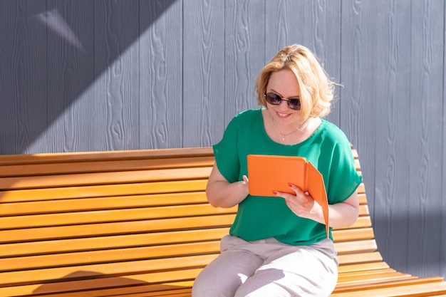 Heureuse femme d'affaires séduisante en lunettes de soleil travaillant à distance dans le parc à l'aide d'un ordinateur portable