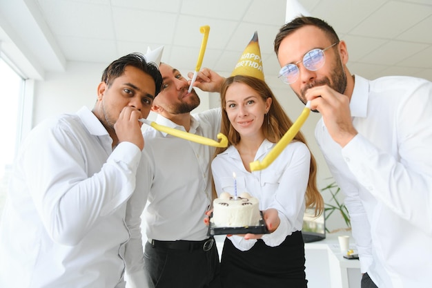 Heureuse femme d'affaires tenant un gâteau d'anniversaire tout en organisant une fête surprise avec ses collègues du bureau