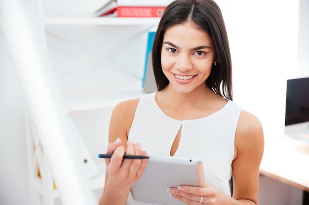 Heureuse femme d'affaires tenant une tablette au bureau et regardant à l'avant