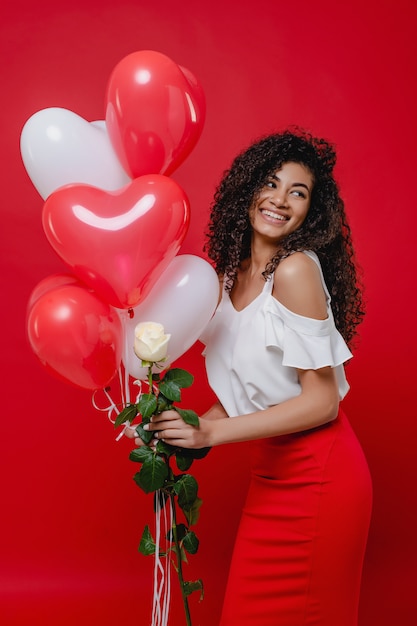 Heureuse femme africaine avec des ballons en forme de coeur et rose blanche