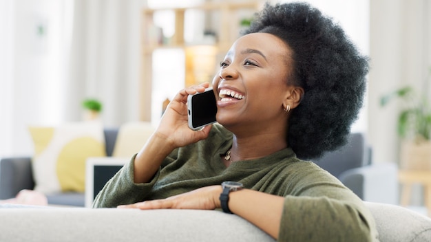 Photo heureuse femme africaine parlant au téléphone tout en se relaxant sur son canapé confortable à la maison joyeuse femme noire avec afro riant tout en ayant une conversation agréable et amusante avec un ami sur son téléphone portable