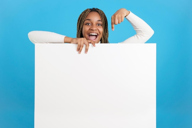 Heureuse femme africaine pointant vers un panneau avec un espace vide