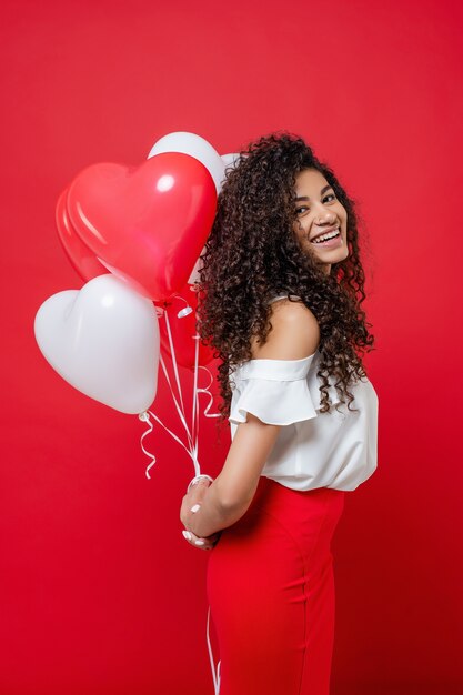 Heureuse femme africaine souriante tenant des ballons colorés à l'hélium derrière son dos