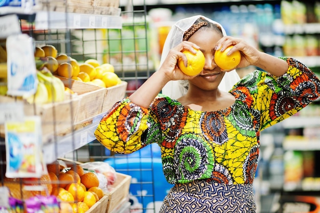 Heureuse femme africaine en vêtements traditionnels et voile à la recherche d'un produit à l'épicerie faisant ses courses dans un supermarché