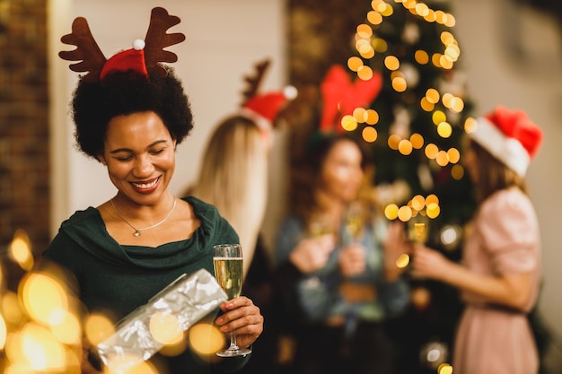 Heureuse femme afro-américaine apportant des cadeaux alors qu'elle célèbre Noël avec ses amis à la fête à la maison.