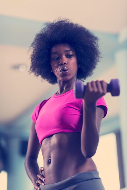 heureuse femme afro-américaine en bonne santé travaillant dans une salle de sport crossfit sur la perte de poids avec des haltères