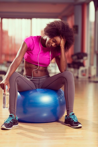 heureuse femme afro-américaine avec une coiffure afro bouclée dans une salle de sport se détendre après l'entraînement de pilates