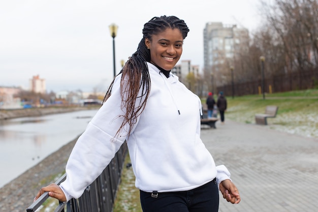 L'heureuse femme afro-américaine dans un parc dans un sweat à capuche blanc