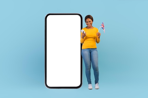 Heureuse femme afro-américaine du millénaire en conversation décontractée sur le téléphone tenir le porte-drapeau de l'angleterre avec grand