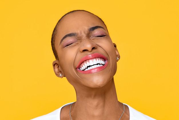 Heureuse femme afro-américaine extatique souriant avec les yeux fermés isolé sur mur jaune coloré