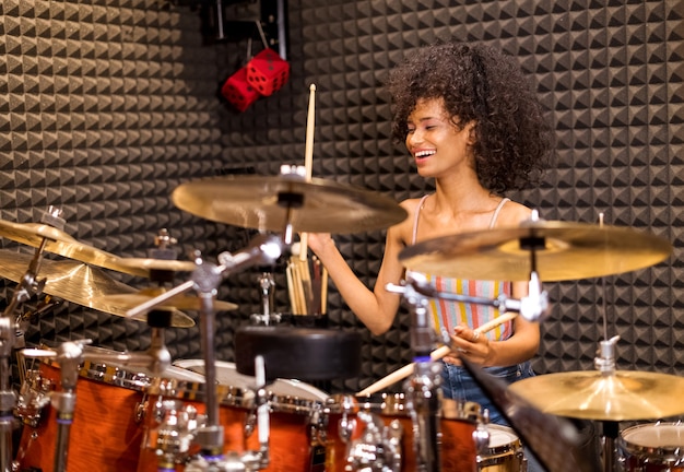 Heureuse femme afro-américaine à jouer de la batterie et des cymbales dans un studio