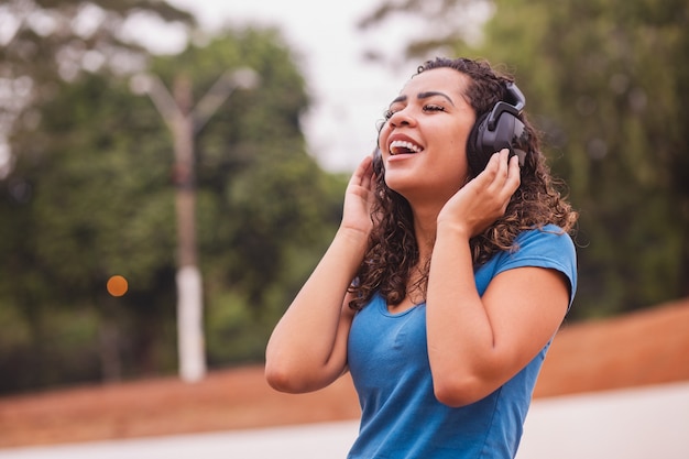 Heureuse femme afro écoutant de la musique sur son casque.