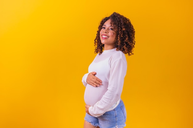Heureuse femme afro enceinte touchant son ventre. Portrait de jeune mère enceinte, caressant son ventre et souriant en gros plan. concept de grossesse en bonne santé