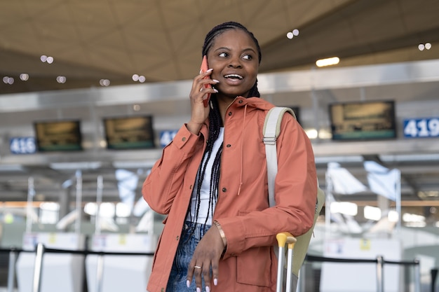 Heureuse femme afro parlant sur smartphone après le premier vol après la fin de la covid et l'arrivée à l'aéroport