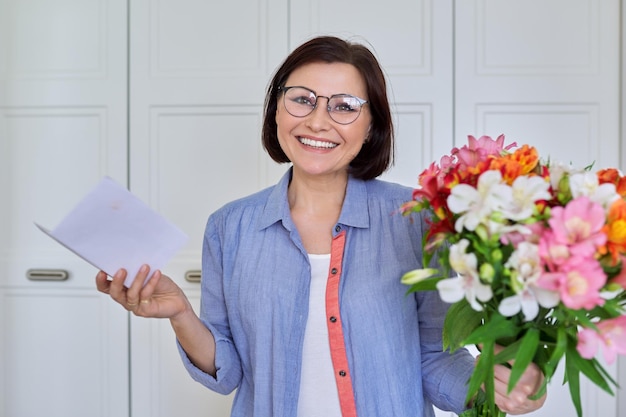 Heureuse femme d'âge moyen avec bouquet de fleurs regardant à huis clos avec félicitations de texte papier