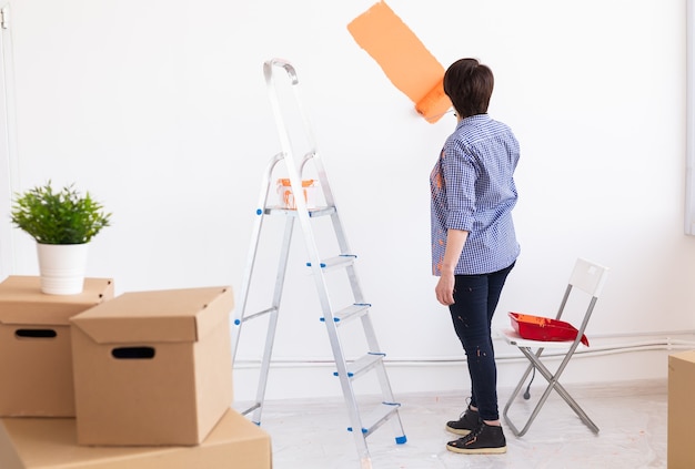 Heureuse femme d'âge moyen peinture mur intérieur avec rouleau à peinture dans la nouvelle maison. Une femme avec rouleau