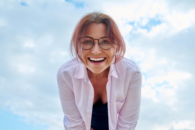 Heureuse femme d'âge moyen regardant le ciel bleu de la caméra sur fond de nuages