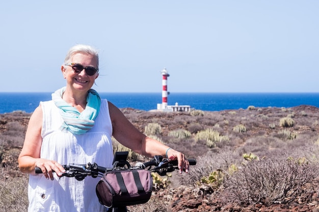 Heureuse femme âgée active aux cheveux blancs utilisant un vélo électrique en mer femme caucasienne âgée dans le phare des vacances d'été à l'horizon