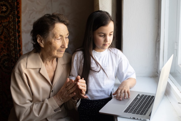 Heureuse femme âgée assise avec sa petite-fille regardant un ordinateur portable faisant un appel vidéo. Dame mûre parlant à la webcam, discutant en ligne à la maison pendant l'auto-isolement. Temps en famille pendant Corona