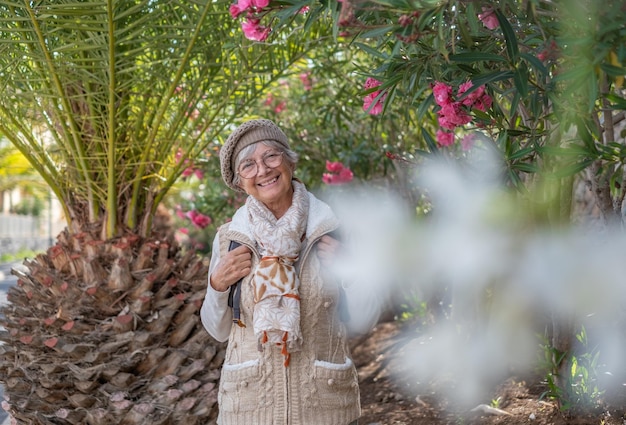 Heureuse femme âgée avec casquette marchant à l'extérieur à l'ombre des plantes