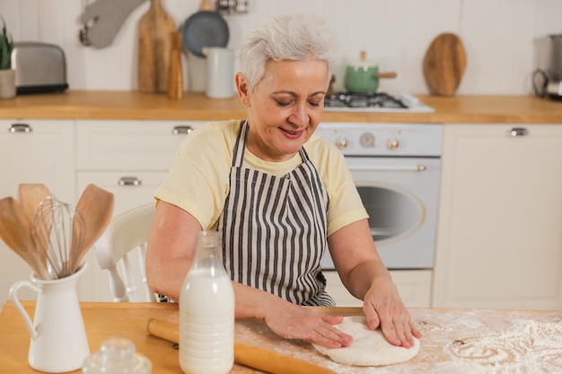 Heureuse femme âgée cuisinant dans une cuisine élégante et mature, dame aux cheveux gris, grand-mère pétrir la pâte