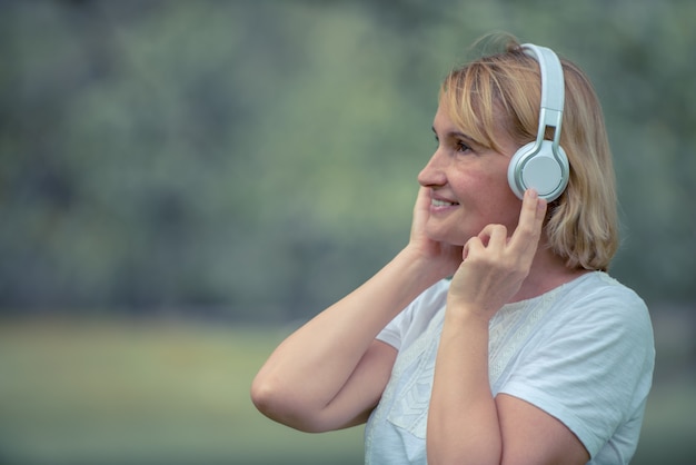 Heureuse femme âgée écoute de la musique sur le casque dans le parc