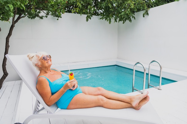 Heureuse femme âgée faisant la fête dans la piscine - Belle femme âgée prenant un bain de soleil et se relaxant dans une piscine privée en été