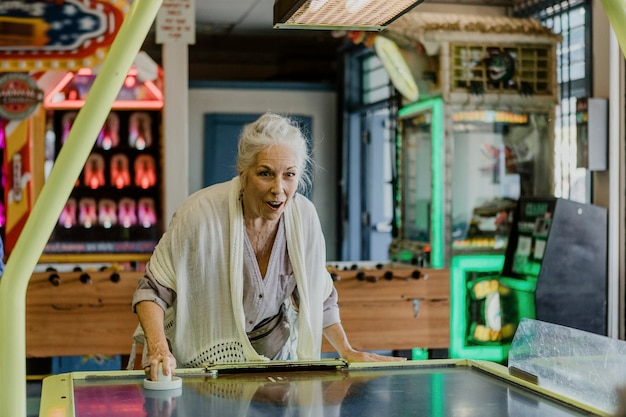 Heureuse femme âgée jouant au hockey sur table à l'arcade