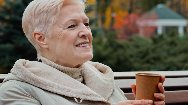 Heureuse femme âgée mature rêveuse aux cheveux gris grand-mère buvant du café thé chaud à partir de jetable