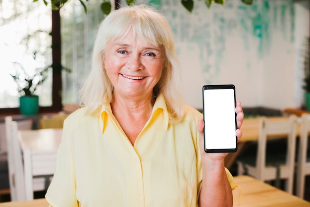 Heureuse femme âgée souriante montrant le smartphone à la caméra