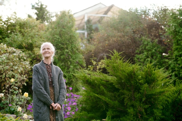 Heureuse femme âgée en tenue décontractée debout parmi les buissons verts et les arbres