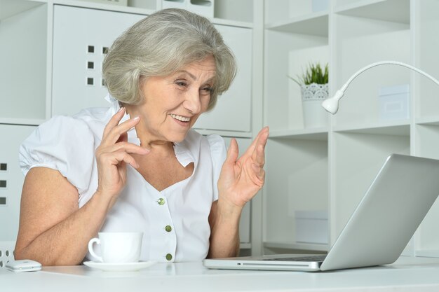 Heureuse femme âgée travaillant sur ordinateur portable au bureau