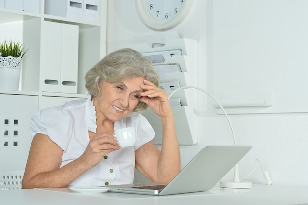 Heureuse femme âgée travaillant sur ordinateur portable au bureau