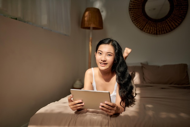 Heureuse femme allongée sur le lit avec tablette et regardant la caméra