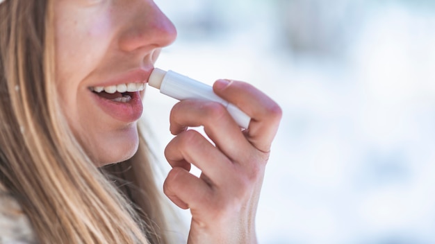 Heureuse femme appliquant un baume pour les lèvres en vacances d&#39;hiver dans une montagne enneigée