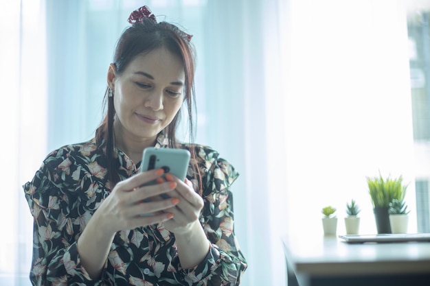 Heureuse femme asiatique à l'aide d'un smartphone Femme souriante à l'aide d'une application shopping en ligne à la maison