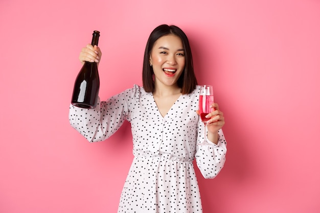 Heureuse femme asiatique célébrant s'amuser et faire la fête en versant une coupe de champagne et en riant debout...