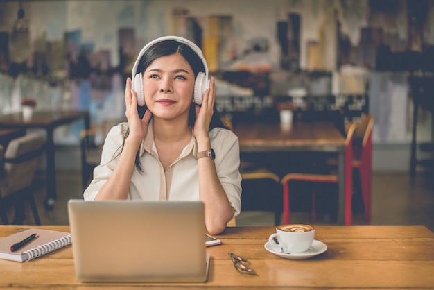 Heureuse femme asiatique détente et écoute de musique au café-restaurant avec ordinateur portable