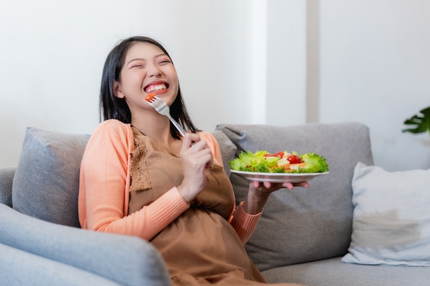 Heureuse Femme Asiatique Enceinte Assis Et Manger Des Aliments Sains De Salade De Légumes Naturels Et Assis Sur Le Canapé