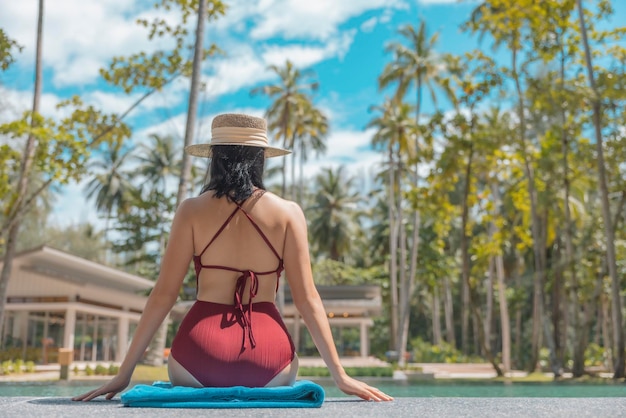 Photo heureuse femme asiatique en maillot de bain rouge et un chapeau de paille relaxant s'asseoir au bord de la piscine à phangnga thaïlande