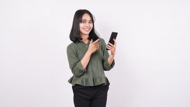 Heureuse femme asiatique pointant le téléphone sur un mur blanc isolé