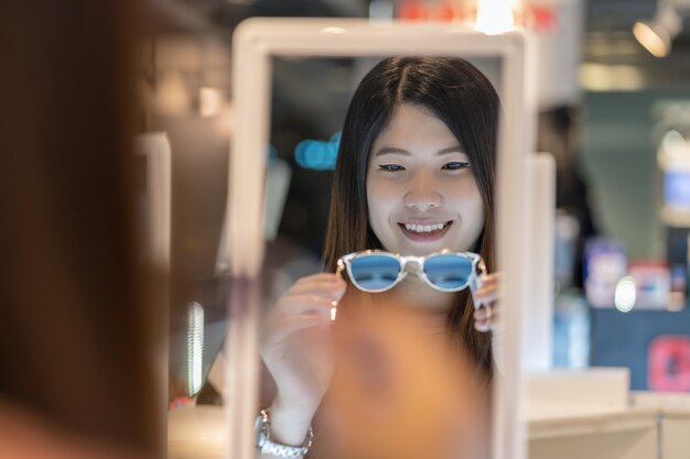 Heureuse femme asiatique à la recherche et en choisissant des lunettes en magasin