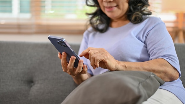 Une heureuse femme asiatique à la retraite de 60 ans utilisant son téléphone sur un canapé dans le salon