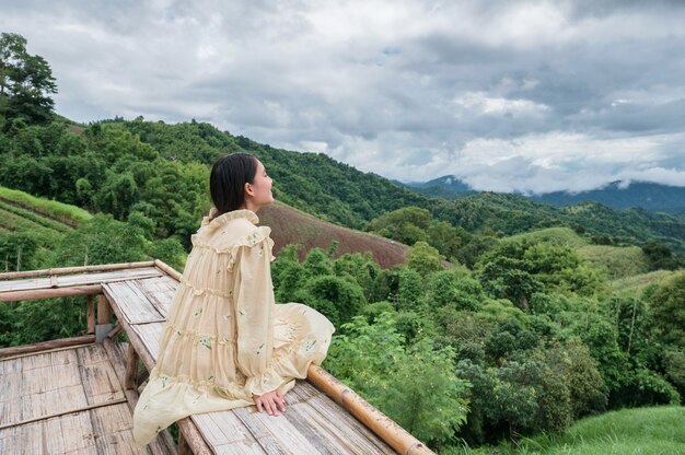 Heureuse Femme Asiatique En Robe Jaune Assise Sur Une Terrasse En Bois Parmi La Montagne En Vacances