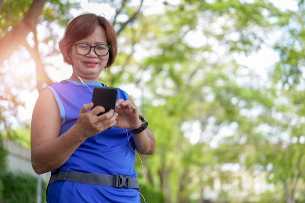 Heureuse femme asiatique senior tenant un téléphone intelligent avec de la musique