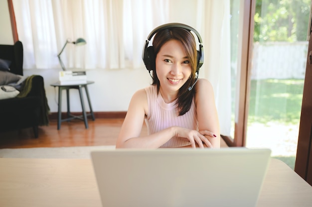 Heureuse femme asiatique souriante portant un casque ayant une vidéoconférence via un ordinateur portable à la maison dans le salon